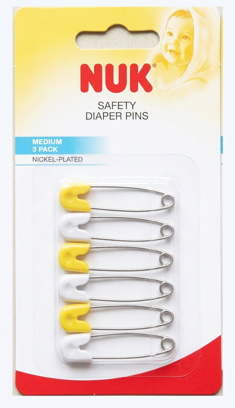 A 3-pack of NUK safety diaper pins in nickel-plated steel with yellow and white plastic tips, packaged in a white, yellow, and red cardboard blister pack.